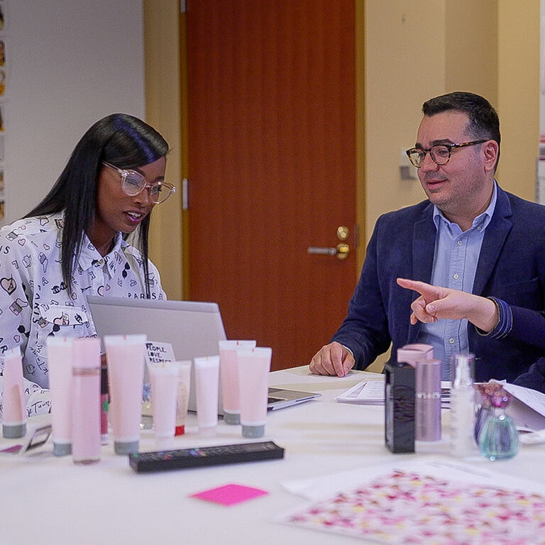 Two people reviewing product packaging designs at a table with skincare tubes and laptop