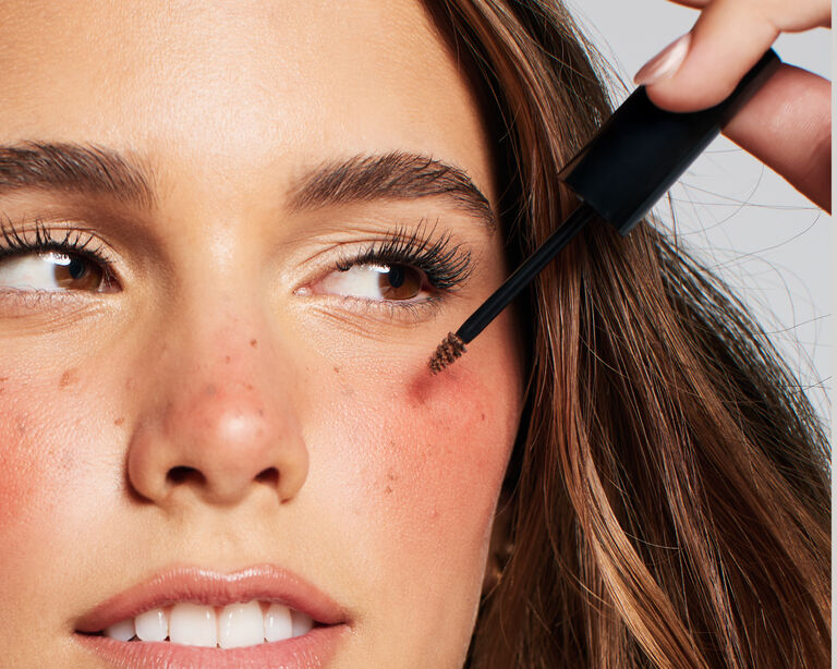 Model applying fake freckles to her cheeks with a brow tint applicator